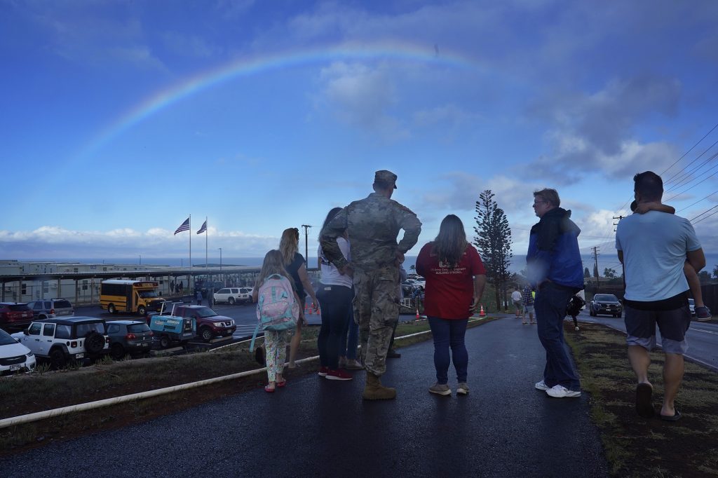 A rainbow forms over supporters and U.S. Army Corps of Engineers recovery field office commander Col. Eric Swenson as they welcome students to the temporary Pulelehua campus of King Kamehameha III Elementary School Monday, April 1, 2024, in Lahaina. Kam 3’s original build was destroyed in the Aug. 8 fire. (Kevin Fujii/Civil Beat/2024)