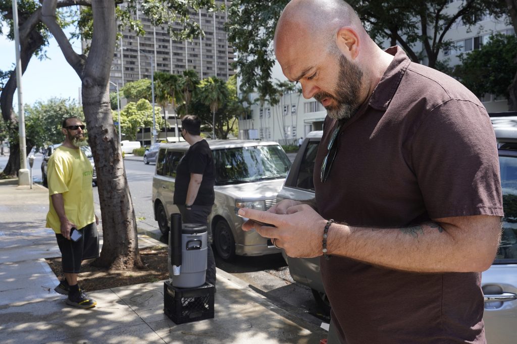 Hawaii Health & Harm Reduction Center’s Michael Salek, from left, and Kourtney Davis stand outside of their van while Joshua Derrig replies to a message at their needle exchange Friday, April 5, 2024, in Honolulu. (Kevin Fujii/Civil Beat/2024)
