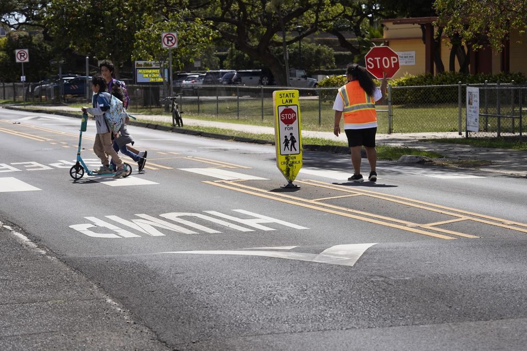 Students cross Papipi Road between speed humps in front of Ewa Beach Elementary School Thursday, March 28, 2024. The tallest student wears an Ilima Intermediate School t-shirt. (Kevin Fujii/Civil Beat/2024)