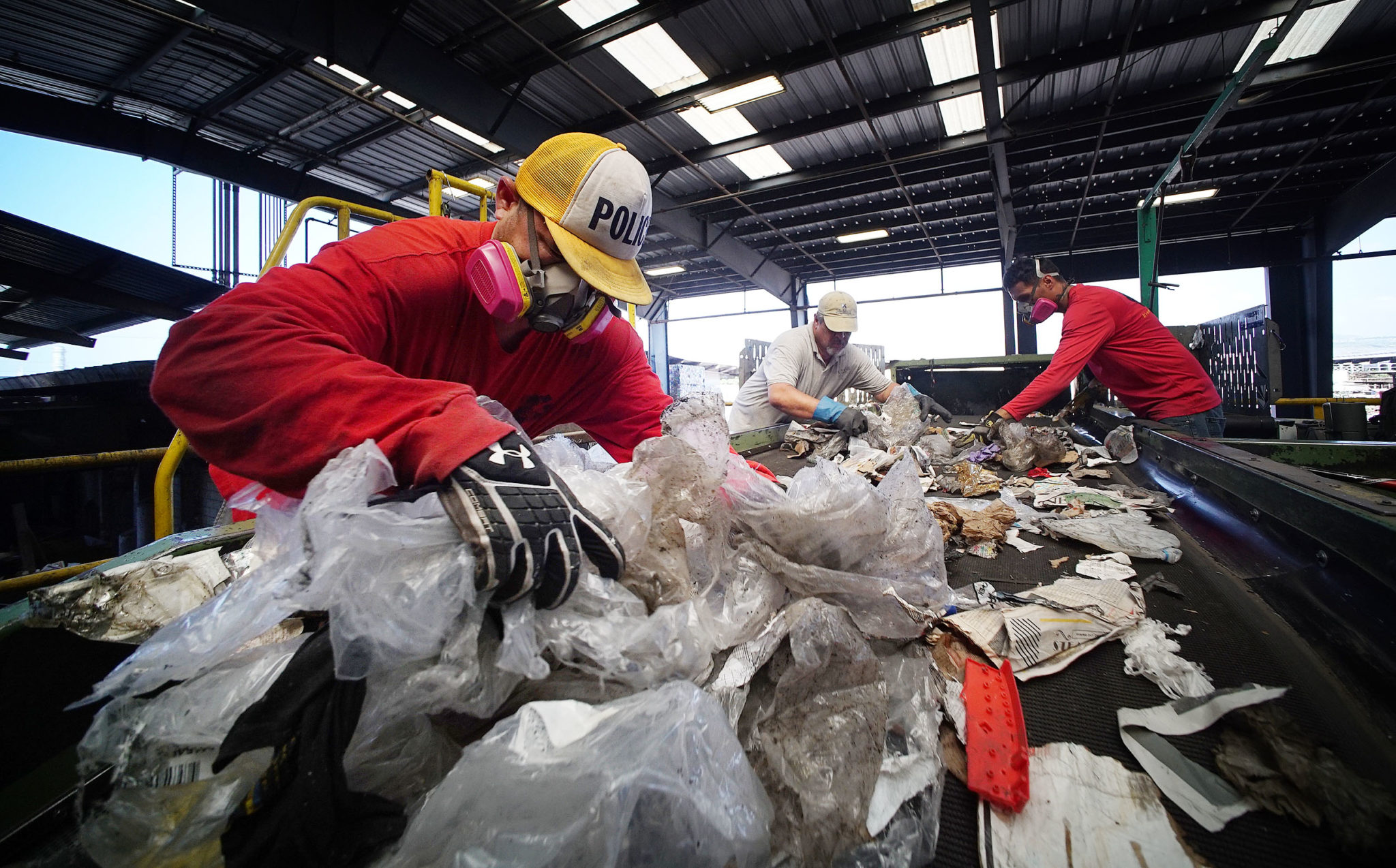 Workers pull plastic off of conveyor belt at RRR Recycling Services Hawaii.