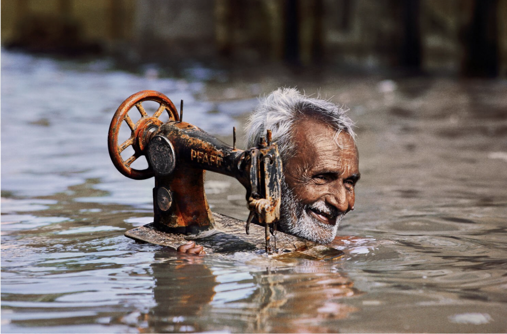 A tailor hoisting his sewing machine on his shoulder to try to rescue it in monsoon floods in Porbandar, India.